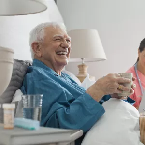 An elderly man seating on his bed in company of a nurse