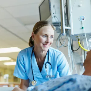 A smiling female physician reassures her male patient in a hospital room.