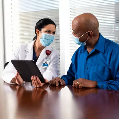 A Doctor Speaks to Her Patient in an Exam Room While Going Over His Charts on a Laptop.