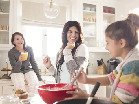 A Caucasian mom dances around the kitchen with her two daughters.