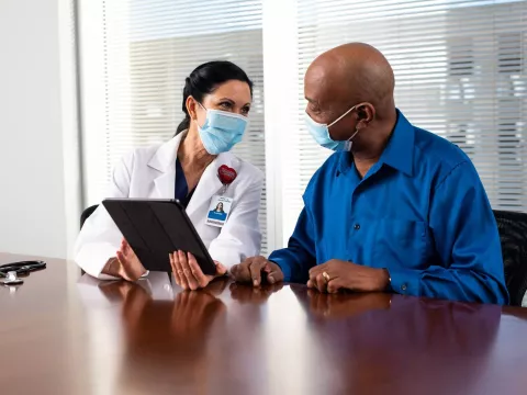 A Doctor Speaks to Her Patient in an Exam Room While Going Over His Charts on a Laptop.