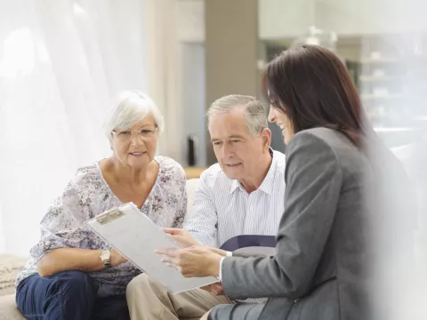 An elderly couple look hopeful as they consult with a female physician holding a clipboard.