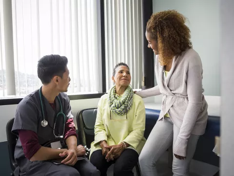An African American daughter consoles her mother upon hearing medical news from the nurse.
