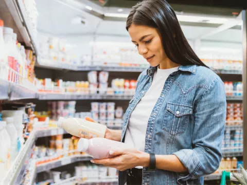 A woman in the dairy aisle of a grocery store holding and looking at bottles.