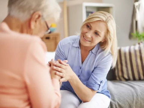A middle-aged woman and her elderly mother hold hands.