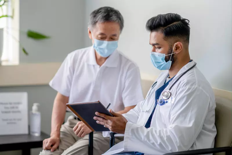A Doctor Reviews a Patient's Chart with Him on a Tablet in an Exam Room.