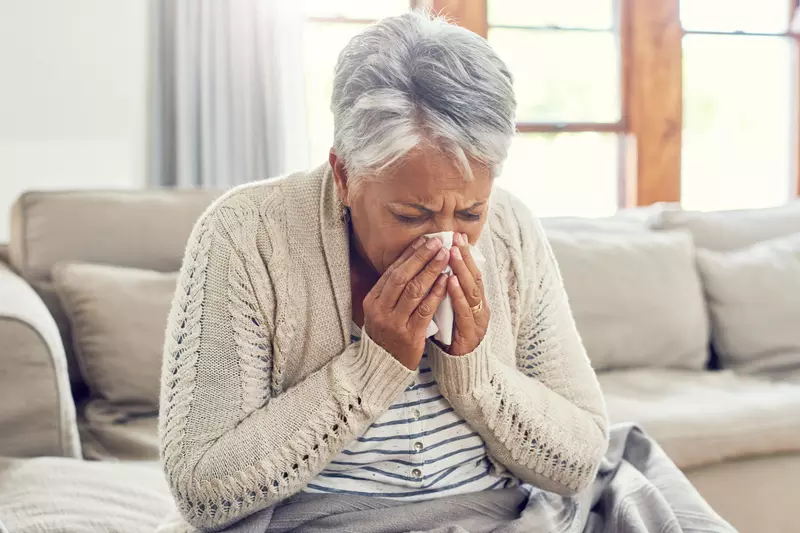 A Senior Woman Blows Her Nose from Seasonal Allergies.