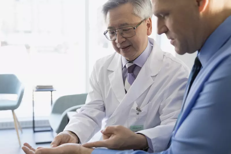 An Asian doctor identifies pain points on a male patient.
