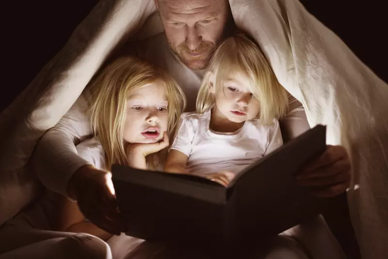 A dad reads to his daughters by flashlight.