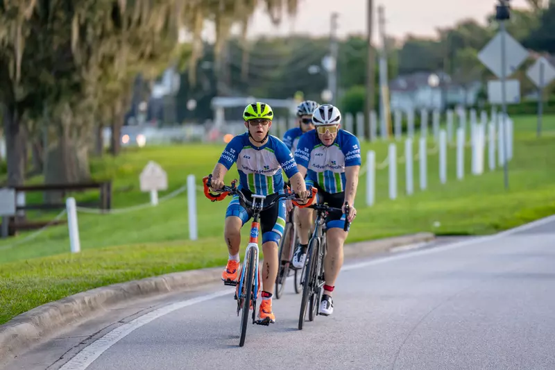 Triathlon participant, Chris Nikic, and his physical therapist, Trevor Hicks, biking on the road