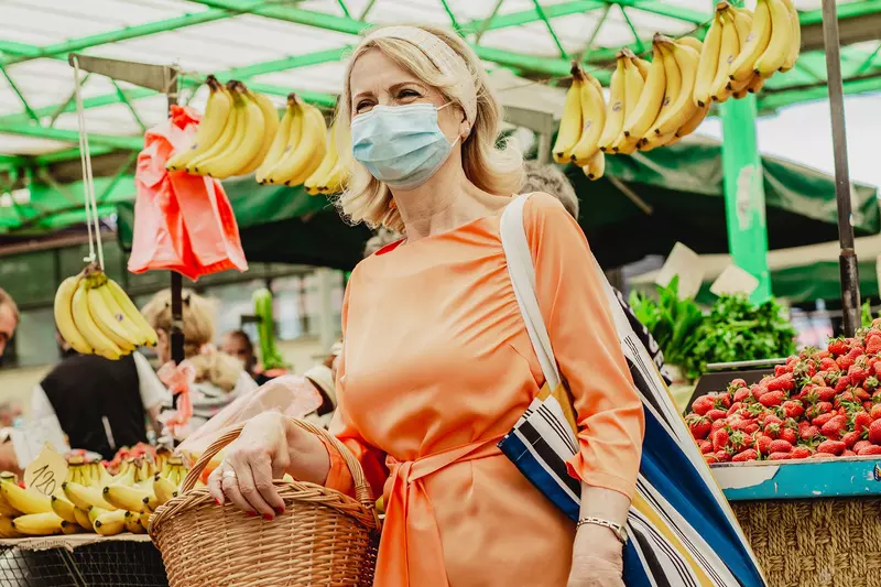 A woman wearing a mask at an outdoor farmers market.