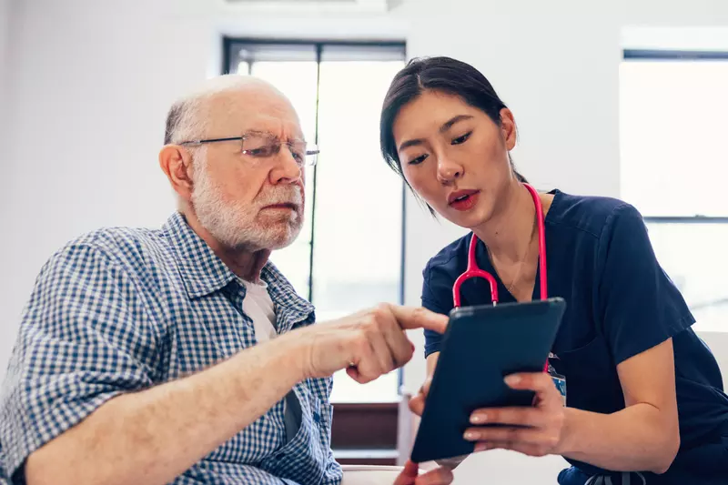 An older man looks at a tablet with a nurse.