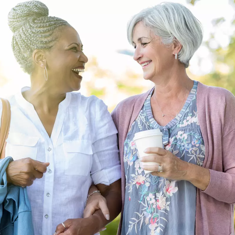 Two healthy mature women enjoy a walk outdoors together.